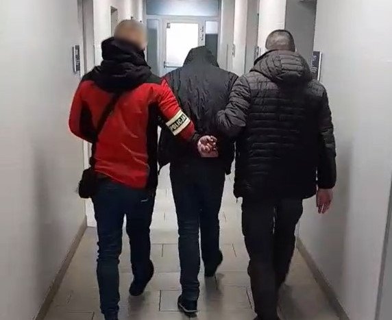 dwóch nieumundurowanych policjantów prowadzi zatrzymanego przez korytarz komisariatu