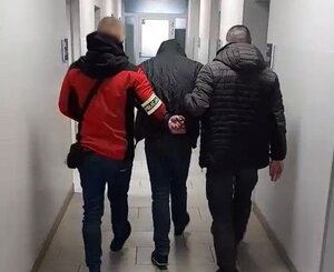 dwóch nieumundurowanych policjantów prowadzi zatrzymanego przez korytarz komisariatu