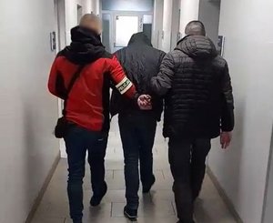 dwóch nieumundurowanych policjantów prowadzi zatrzymanego przez korytarz komisariatu