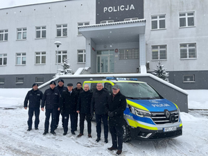 wspólne zdjęcie przedstawicieli władz samorządowych z policjantami na tle radiowozu i komendy