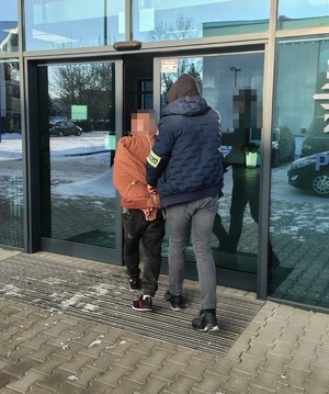 nieumundurowany policjant prowadzi zatrzymanego do siedziby komendy