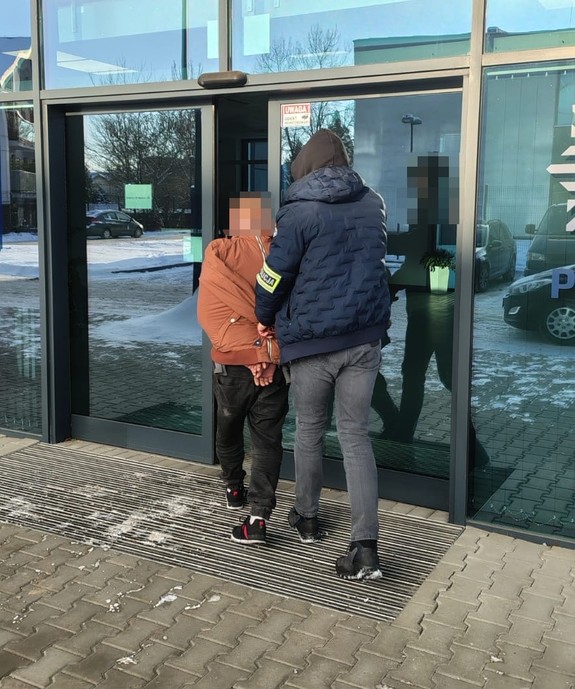 nieumundurowany policjant prowadzi zatrzymanego do siedziby komendy