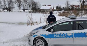 Policyjny radiowóz oraz policjant stojący przed zamarzniętym akwenem wodnym