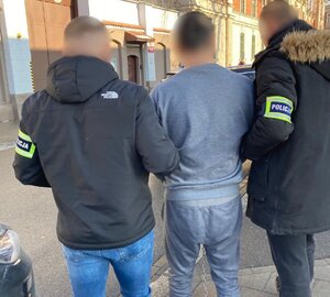 dwóch nieumundurowabych policjantów prowadzi zatrzymanego mężczyznę do aresztu śledczego