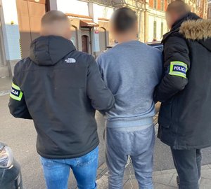 dwóch nieumundurowabych policjantów prowadzi zatrzymanego mężczyznę do aresztu śledczego