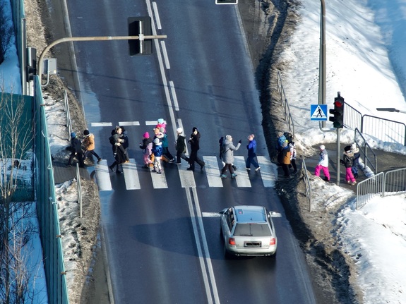 Grupa dzieci przechodzi przez przejście dla pieszych. Przed przejściem stoi samochód