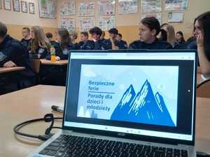 Laptop z otwartą prezentacją zatytuowaną Bezpieczne Ferie oraz uczniowie klasy o profilu policyjnym