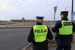 7 KPP Oświęcim. Zabezpieczenie 81. rocznicy wyzwolenia Auschwitz-Birkenau policjantka i policjant przy ulicy w tle Brama Śmierci