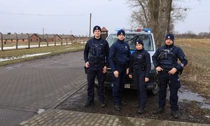 5 KPP Oświęcim. Zabezpieczenie 81. rocznicy wyzwolenia Auschwitz-Birkenau    policjanci przy radiowozie w tle Birkenau