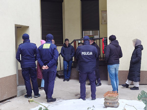 Policjant i strażnicy miejscy rozmawiają we wnece budynku ze zgromadzonymi osobami