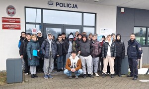 Na tle budynku komendy grupa osób i policjant