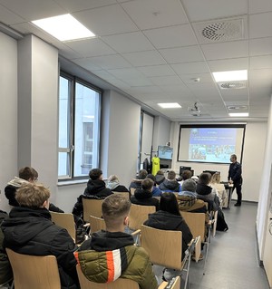 Osoby siedzące na krzesłach, przed nimi policjant który wyświetla prezentację.