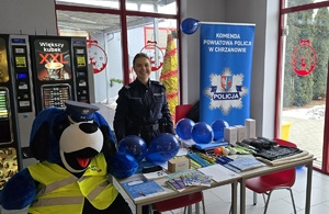 Policjantka stoi przy stoisku, obok niej siedzi maskotka KPP Chrzanów „Poluś”