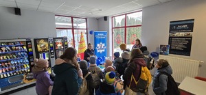 Na pierwszym planie grupa dzieci, wraz z opiekunami, stojąca przed stoiskiem, dalej stojąca policjantka