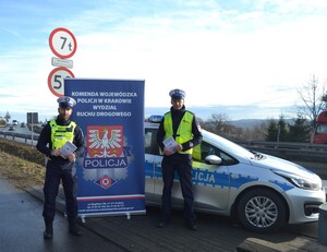 Policjanci stojący obok radiowozu, trzymający broszurki z akcji