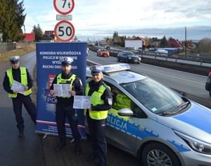 Policjanci stojący przy radiowozie, trzymający broszurki z akcji