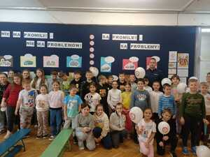 Policjant stoi razem z dziećmi na tle gazetki szkolnej o tematyce akcji No promil No problem