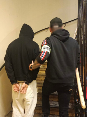 nieumundurowany policjant prowadzi zatrzymanego po schodach z założonymi kajdankami na rękach trzymanych z tyłu