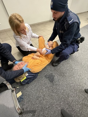 kobiet alezaca na podlodze obok dwoch policjantow jeden z nich trzyma fantoim noworodka na rekach