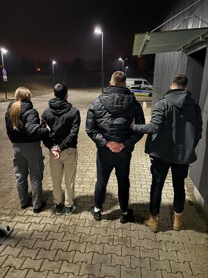 policjanci bez mundurów stoją trzymając zatrzymanych przed budynkiem komendy