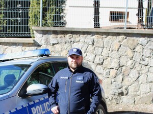 Piotr Kiliański w policyjnym mundurze przy radiowozie