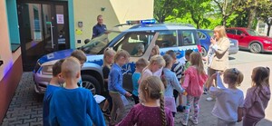 dzielnicowy mł.asp. Marcin Kowalski stoi koło radiowozu wśród dzieci