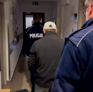 Osoba zatrzymana prowadzona przez umundurowanych policjantów przez korytarz