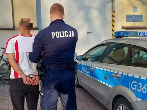 Policjant trzymający zatrzymanego mężczyznę, po prawej stronie radiowóz