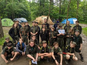 grupa harcerzy wraz z policjantem pozująca do zdjęcia na terenie obozowiska w lesie