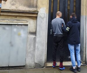 nieumundurowany policjant prowadzi zatrzymanego do budynku komisariatu