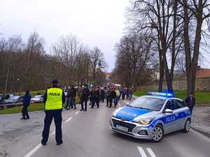 Policjant stojący tyłem, po prawej stronie radiowóz i tłum osób