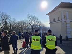 Dwaj policjanci w odblaskowych kamizelkach stojący tyłem, przed nimi tłum ludzi