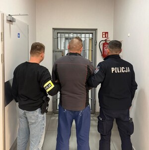 poszukiwany mężczyzna stoi z dwoma policjantami przed policyjną celą