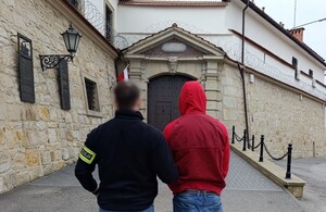 nieumundurowany policjant prowadzi zatrzymanego do zakładu karnego