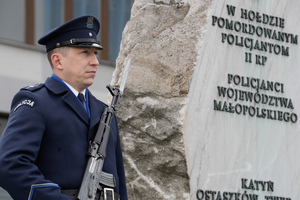 Policjant stojący przy obelisku pamiątkowym na terenie KWP Kraków
