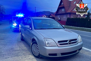 srebrny opel a za nim policyjny radiowóz z włączonymi niebieskimi światłami błyskowymi