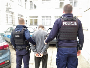 dwóch umundurowanych policjantów prowadzi zatrzymanego mężczyznę