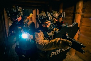 trzech kontrterrorystów w układzie bojowym z tarczą i latarkami