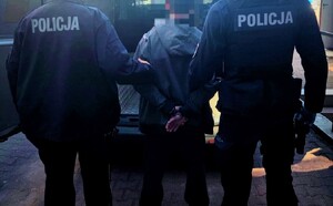 Dwóch policjantów, a pośrodku zatrzymany mężczyzna. Osoby są tyłem