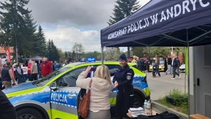 Na tle namiotu i radiowozu policjantka oraz kobieta. W tle tłum osób