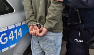 ZATRZYMANY MĘŻCZYZNA Z ZAŁOŻONYMKI KAJDANKAMI NA RĘKACH TRZYMANYCH Z TYŁU.