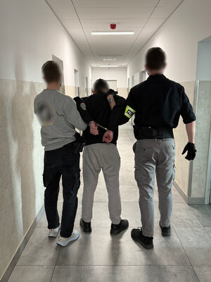 dwóch nieumundurowanych policjantów prowadzi zatrzymanego z kajdankami założonymi na ręce trzymane z tyłu