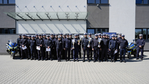 Liczna grupa policjantów biorących udział w konkursie policjant ruchu drogowego wraz z przełożonymi, stoją pomiędzy motocyklami policyjnymi