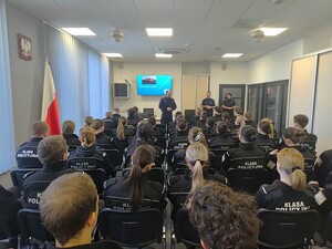 Dwóch policjantów i policjantka oraz grupa uczniów siedzących przed nimi na krzesłach
