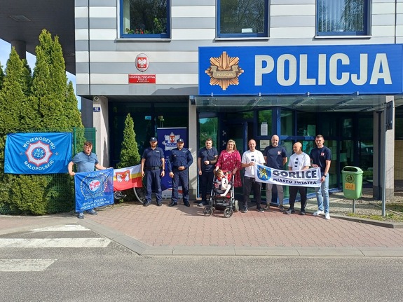 Przed komendą Policji w Gorlicach stoją uczestnicy rajdu charytatywnego wraz z dwoma policjantami oraz dzieckiem na wózku i jego rodzicami