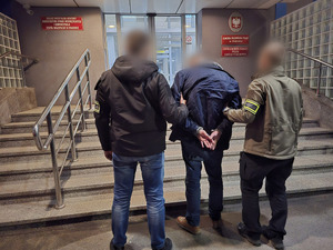 zatrzymany prowadzony przez policjantów przed komendą