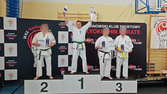 Zawodnicy karate w strojach sportowych. Zawodnicy stoją na podium trzymając w rękach pamiątkowe dyplomy i statuetki