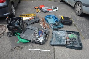 Skrzynki narzędziowe o różnej wielkości, w których znajdują się elektronarzędzia. Pomiędzy skrzynkami metalowe pręty.