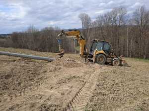 Koparka CAT z zamontowany na ramieniu świdrem. Obok leży betonowy słup energetyczny