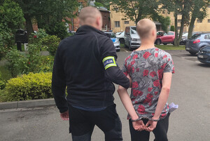 nieumundurowany policjant prowdzi zatrzymanego z założonymi kajdankami na ręce trzymane z tyłu